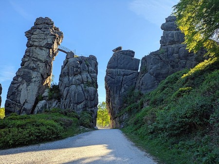 Felsformationen der Externsteine im Sommerlicht mit einem Weg zwischen den Felsen und grüner Vegetation.