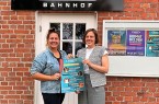Doreen Belhaouès und Jana Felmet stehen vor dem Weberei-Bahnhof und halten ein Plakat zum Kinderprogramm.