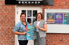 Doreen Belhaouès und Jana Felmet stehen vor dem Weberei-Bahnhof und halten ein Plakat zum Kinderprogramm.