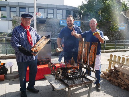 Drei Männer bereiten am Grill Flammlachs und Fischbrötchen beim Fischerfest in Bad Lippspringe zu.