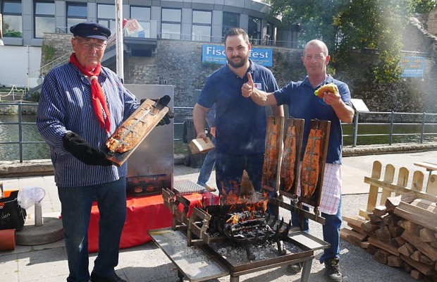 Drei Männer bereiten am Grill Flammlachs und Fischbrötchen beim Fischerfest in Bad Lippspringe zu.