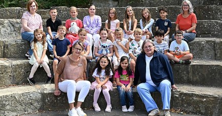 Teilnehmende Kinder und vier Erwachsene von FIT in Deutsch an der Josefschule Büren sitzen für ein Gruppenfoto auf Steinstufen.