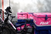 Flink-Lieferfahrräder mit pink-blauen Transportboxen stehen nebeneinander.