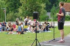 Poetry-Slammer auf einer kleinen Freiluftbühne vor einem auf Decken sitzenden Publikum auf einer Wiese.