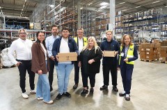 Gruppenfoto der IHK-Ausbildungstour bei SK Pharma Logistics in einer Lagerhalle in Bielefeld; zwei junge Beschäftigte halten Pakete.
