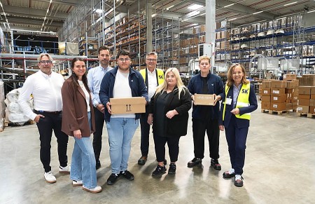 Gruppenfoto der IHK-Ausbildungstour bei SK Pharma Logistics in einer Lagerhalle in Bielefeld; zwei junge Beschäftigte halten Pakete.