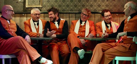Die sechs Musiker der Jazz Connection sitzen in orangefarbenen Anzügen gemeinsam in einem Clubraum.