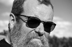 Schwarz-Weiß-Porträt eines bärtigen Mannes mit Sonnenbrille im Freien.