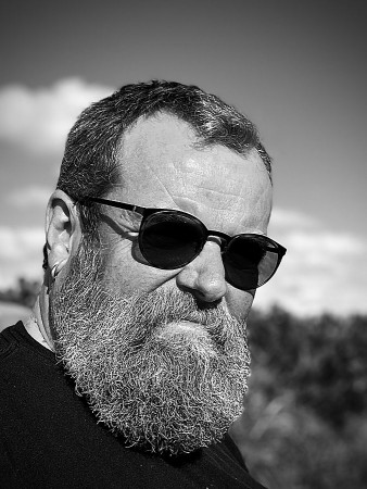 Schwarz-Weiß-Porträt eines bärtigen Mannes mit Sonnenbrille im Freien.