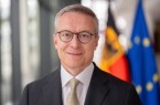 Porträt eines Mannes im Anzug vor unscharf dargestellter deutscher und europäischer Flagge.