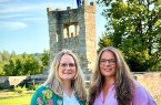 Zwei Frauen stehen auf einer Grünfläche vor einem steinernen Turm mit Europaflagge.