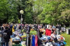 Gut besuchter Flohmarkt im Grünen mit Kleiderständern, Tischen, Spielzeug und zahlreichen Besucherinnen und Besuchern.