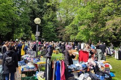 Gut besuchter Flohmarkt im Grünen mit Kleiderständern, Tischen, Spielzeug und zahlreichen Besucherinnen und Besuchern.