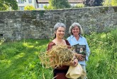 Zwei Frauen im Abteigarten Marienmünster, eine mit einem Krautbund und die andere mit einem Buch.