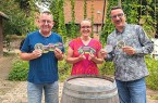 Drei Personen mit bedruckten Bierdeckeln der Bürgerbrauzunft Nieheim vor einem Holzfass.