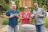 Drei Personen mit bedruckten Bierdeckeln der Bürgerbrauzunft Nieheim vor einem Holzfass.