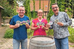 Drei Personen mit bedruckten Bierdeckeln der Bürgerbrauzunft Nieheim vor einem Holzfass.