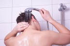 Person spült beim Duschen die Haare mit einer Handbrause unter fließendem Wasser.