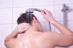 Person spült beim Duschen die Haare mit einer Handbrause unter fließendem Wasser.