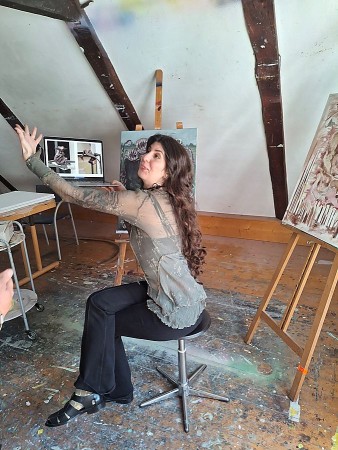 Linda Marwan sitzt in ihrem Atelier im Künstlerhaus Schwalenberg vor Gemälden und einem Laptop mit digitalen Entwürfen.