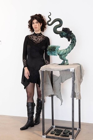 Linda Marwan steht neben einer grün-schwarzen hybriden Skulptur auf einem Metalltisch.