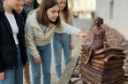 Fünf Kinder und Jugendliche betrachten eine kleine Märchenfigur, die auf einem Stapel Bücher sitzt.