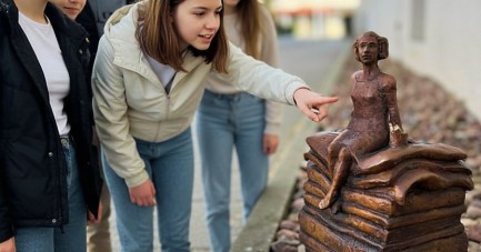 Fünf Kinder und Jugendliche betrachten eine kleine Märchenfigur, die auf einem Stapel Bücher sitzt.