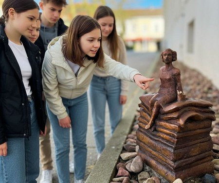 Fünf Kinder und Jugendliche betrachten eine kleine Märchenfigur, die auf einem Stapel Bücher sitzt.
