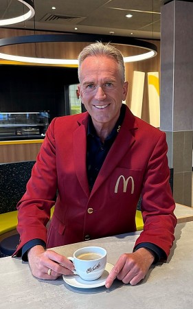 Mann in rotem McDonald's-Sakko mit einer McCafé-Tasse im modernisierten Restaurant.