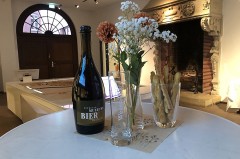 Flasche Mindener Museumsbier mit Biergläsern, Blumen und Gebäck im Ausstellungsraum des Mindener Museums.
