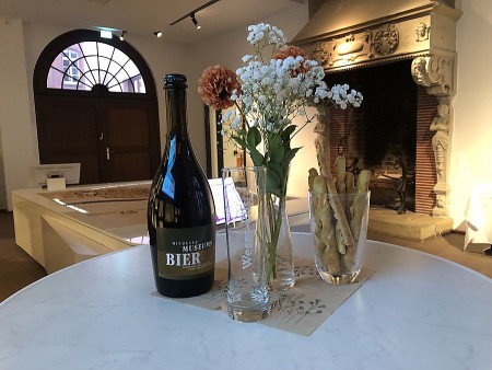 Flasche Mindener Museumsbier mit Biergläsern, Blumen und Gebäck im Ausstellungsraum des Mindener Museums.