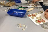 Arbeitstisch mit Perlen, Ohrringen, Modelliermaterial, Blütenanhängern und Werkzeugen bei einem Schmuckworkshop.