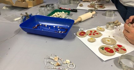 Arbeitstisch mit Perlen, Ohrringen, Modelliermaterial, Blütenanhängern und Werkzeugen bei einem Schmuckworkshop.
