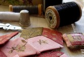 Nähutensilien mit Garnrollen, Fingerhut, Schere und handgenähten Stoffstücken in Rot- und Rosatönen
