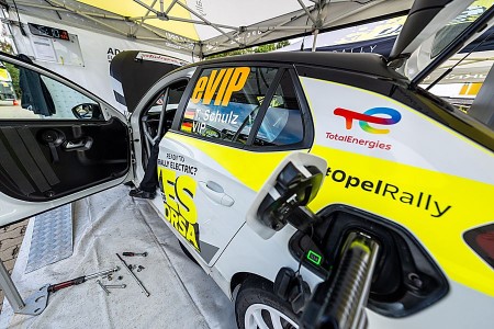 Weiß-gelber Opel Mokka GSE Rally mit geöffneten Türen und Ladeanschluss in einem Servicezelt.