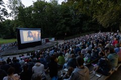 Zahlreiche Besucherinnen und Besucher sitzen im Mohns Park vor einer großen Leinwand bei einer Open-Air-Kinovorführung.