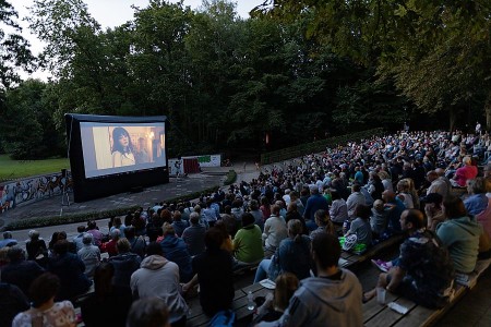 Zahlreiche Besucherinnen und Besucher sitzen im Mohns Park vor einer großen Leinwand bei einer Open-Air-Kinovorführung.
