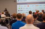 Publikum bei einer SICP-Veranstaltung vor einer Präsentation mit Logos von Mitgliedsunternehmen.