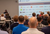 Publikum bei einer SICP-Veranstaltung vor einer Präsentation mit Logos von Mitgliedsunternehmen.