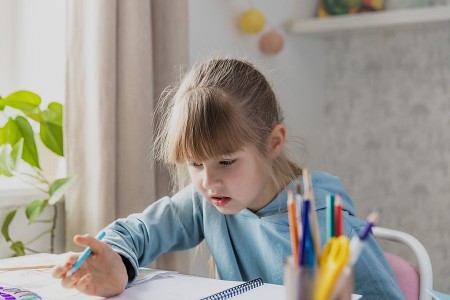 Ein Mädchen sitzt an einem Tisch und zeichnet mit einem Stift in einem Heft.