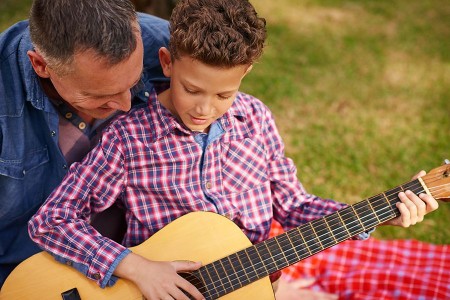 Ein Mann zeigt einem Jungen im Freien das Spielen einer Akustikgitarre.