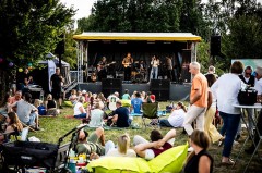 Band auf der Bühne beim Picknick-Konzert an der Krullsbachaue vor sitzendem Publikum © Matheus Fernandes
