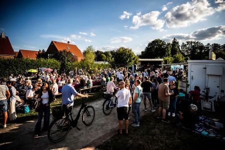 Zahlreiche Besucher*innen beim Picknick-Konzert an der Krullsbachaue mit Bühne und Sitzbänken im Hintergrund © Matheus Fernandes