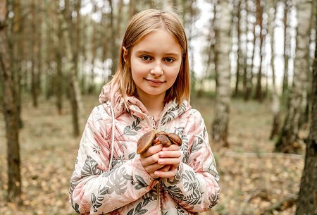 Ein Mädchen steht im Wald und hält mehrere gesammelte Pilze in beiden Händen.