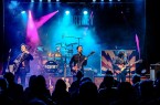 Vierköpfige Band ReCartney spielt mit Gitarren und Schlagzeug auf einer blau und pink beleuchteten Bühne vor Publikum.