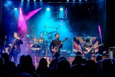 Vierköpfige Band ReCartney spielt mit Gitarren und Schlagzeug auf einer blau und pink beleuchteten Bühne vor Publikum.