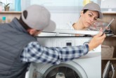Servicetechniker und Kundin prüfen gemeinsam eine geöffnete Waschmaschine während einer Reparatur. 
© Foto: Verbraucherzentrale NRW