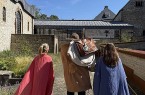 Drei Personen in römisch anmutenden Gewändern stehen im Innenhof des LWL-Museums in der Kaiserpfalz in Paderborn.