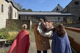 Drei Personen in römisch anmutenden Gewändern stehen im Innenhof des LWL-Museums in der Kaiserpfalz in Paderborn.