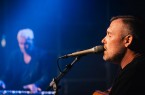 Sebastian Hegener singt bei einem Auftritt in ein Mikrofon und spielt Gitarre.
